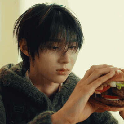 Young Man In Green Sweater Eating Hamburger With Lettuce And Tomato GIF