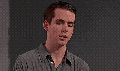 Young Man In Grey Shirt Against Black Wall GIF
