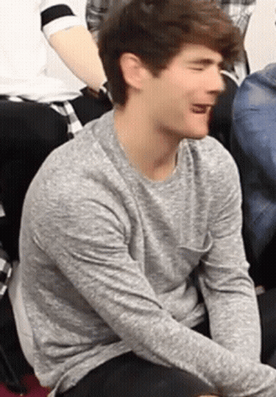 Young Man In Grey Sweater Sitting With Tongue Out GIF