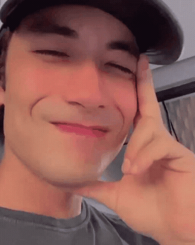 Young Man In Hat Making Funny Face With Hand On Face GIF