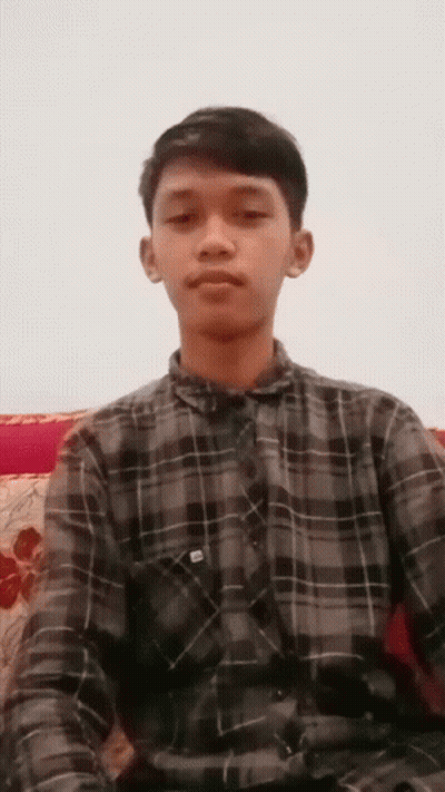 Young Man In Plaid Shirt Sitting On Couch Looking At Camera GIF