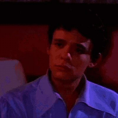 Young Man In Purple Shirt Sitting In Dark Room GIF