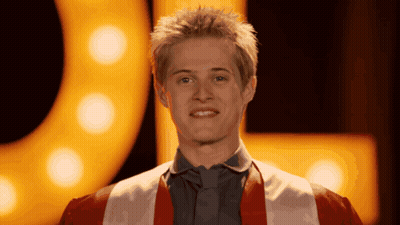 Young Man In Red And White Robe Smiling In Front Of Yellow Sign GIF