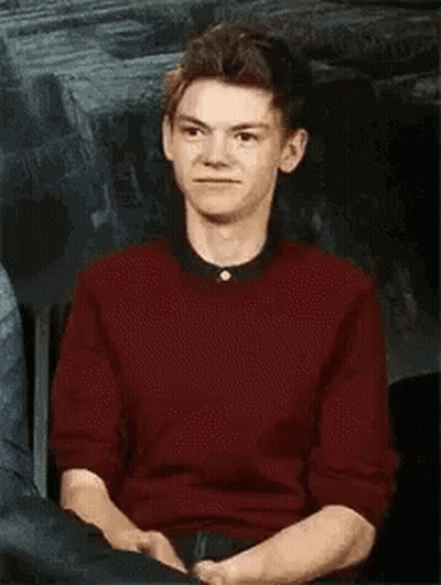 Young Man In Red Sweater Sitting With Hands Folded GIF