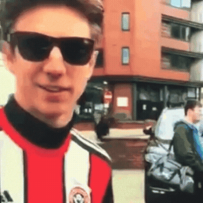 Young Man In Sunglasses And Striped Shirt Standing In Front Of Building GIF