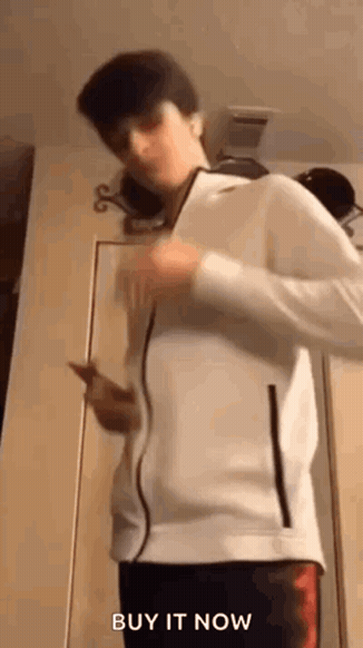 Young Man In White Jacket Holding Cell Phone By Door GIF