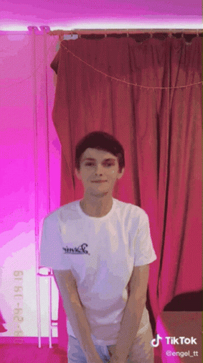 Young Man In White Shirt In Front Of Pink Curtain With TikTok GIF