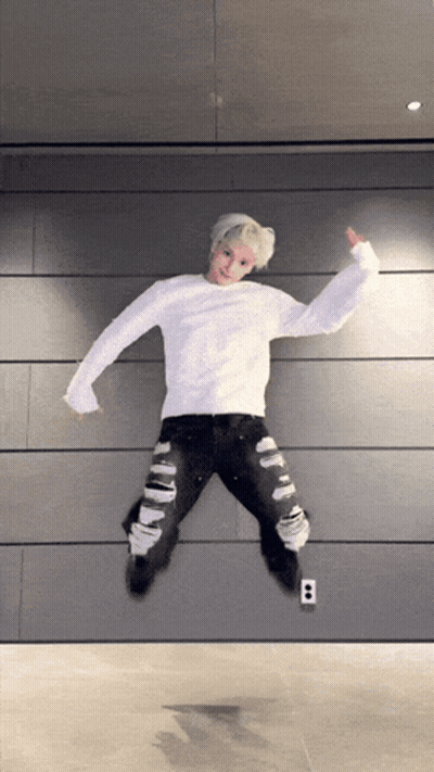 Young Man In White Sweater Jumping In Ripped Jeans GIF