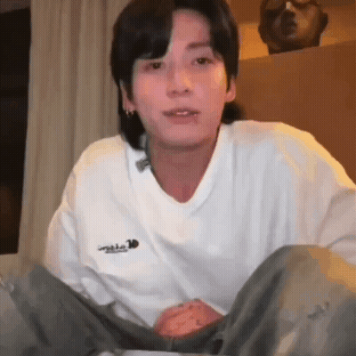 Young Man In White Sweater Sitting On Bed GIF