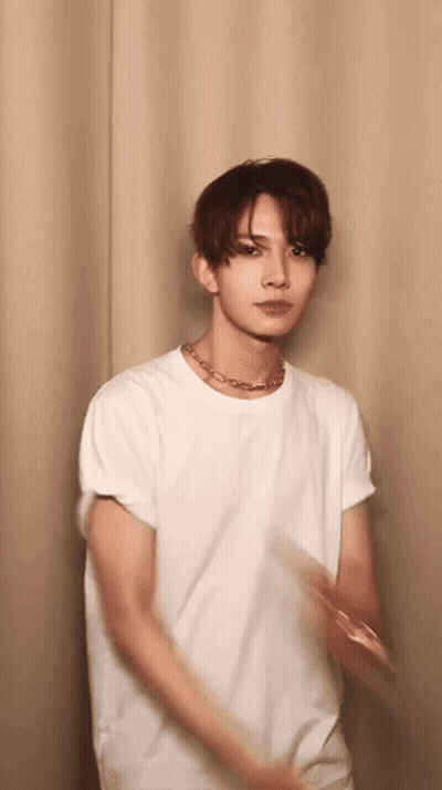 Young Man in White T-Shirt and Necklace Standing Before Curtain