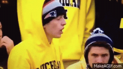 Young Man In Yellow Hoodie And Hat Sitting In Crowd GIF