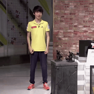 Young Man In Yellow Shirt In Front Of Brick Wall And Toy Display GIF