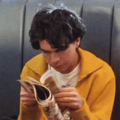 Young Man In Yellow Sweater Reading Magazine GIF