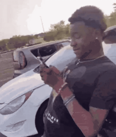 Young Man Looking At Phone In Front Of White Car GIF