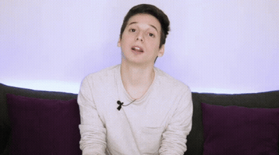Young Man On Couch With Purple Pillows Gesturing GIF