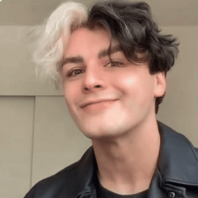 Young Man With Black And White Hair Smiling In Black Jacket GIF