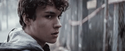 Young Man With Curly Hair In Grey Hoodie Looking At Camera GIF
