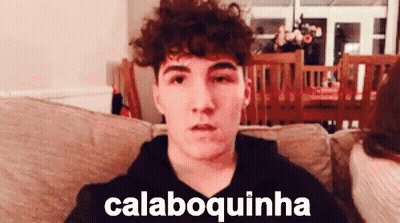 Young Man With Curly Hair Sitting On Couch Saying Calaboquinha GIF