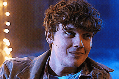 Young Man With Curly Hair Smiling In Front Of Blue Background With Lights GIF