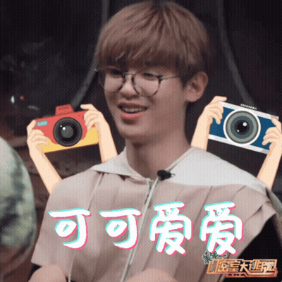 Young Man With Glasses Holding Two Cameras With Chinese Writing GIF