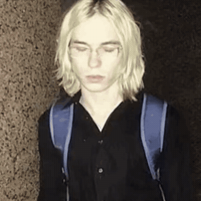 Young Man With Long Blonde Hair And Blue Backpack GIF