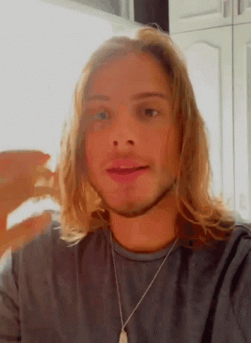 Young Man With Long Blonde Hair In Gray Shirt And Necklace GIF