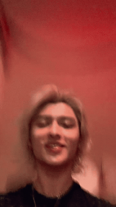 Young Man With Long Blonde Hair Smiling In Black Shirt GIF