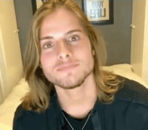 Young Man With Long Hair And Beard Sitting On Bed GIF