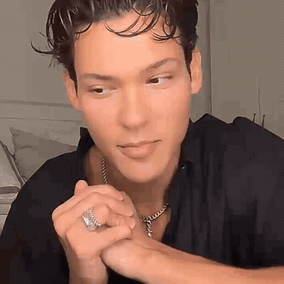 Young Man With Necklace And Ring Sitting In Room GIF