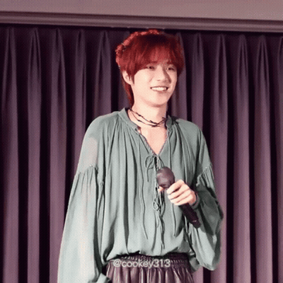 Young Man With Red Hair Holding Microphone Smiling In Front Of Purple Curtain GIF