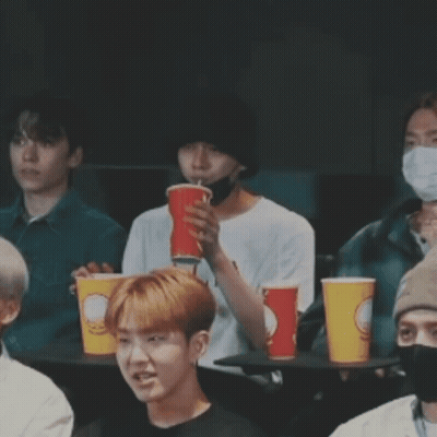 Young Men At Table With Cups, One Covering Mouth GIF