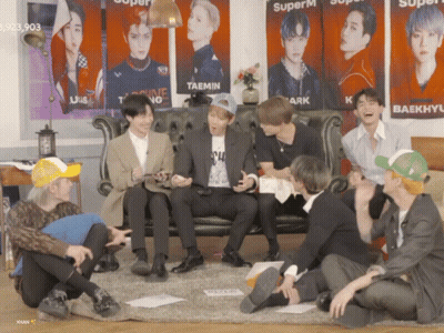 Young Men Sitting On Floor In Front Of Couch With Superm Posters GIF