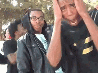 Young Men Standing, One Covering Face GIF