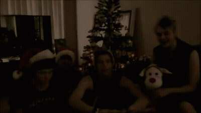 Young Men Wearing Santa Hats By Christmas Tree GIF