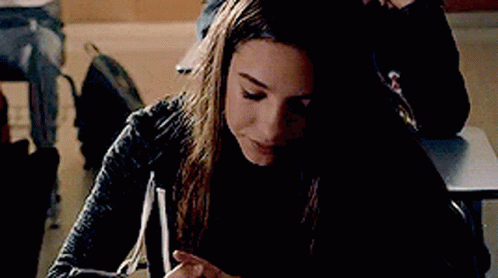 Young Woman Sitting At Desk Looking At Phone GIF