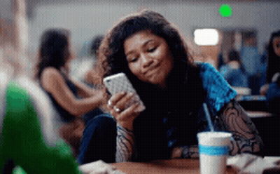 Young Woman Sitting At Table Looking At Cell Phone GIF