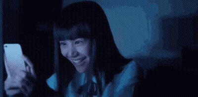 Young Woman Smiling At Phone In Dark GIF