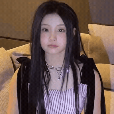 Young Woman With Long Black Hair Sitting On Couch In Striped Top And Necklace GIF
