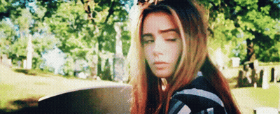 Young Woman With Red Hair Sitting In Cemetery Eyes Closed GIF